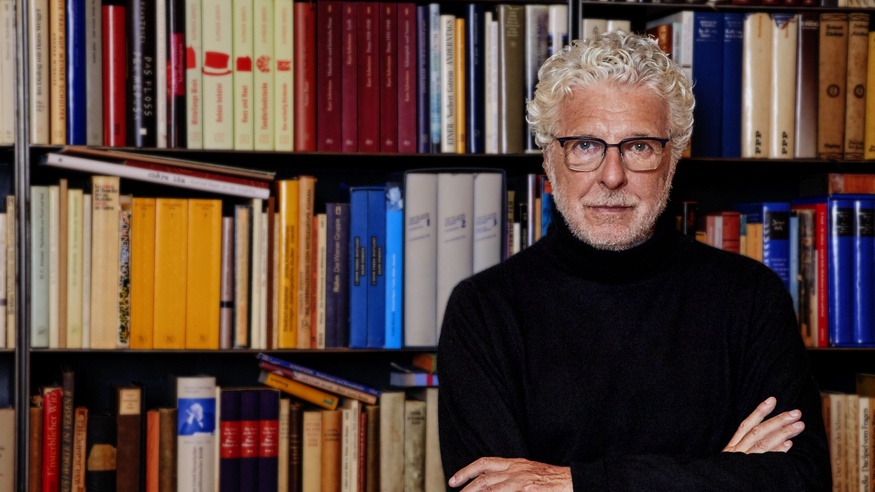 André Heller vor einem Bücherregal