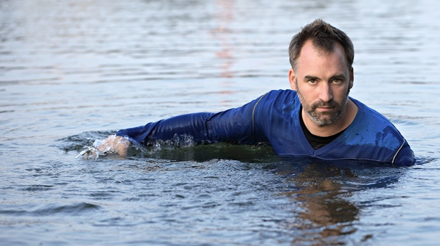 Bernhard Fleischmann mit blauem Gewand liegend im Wasser.